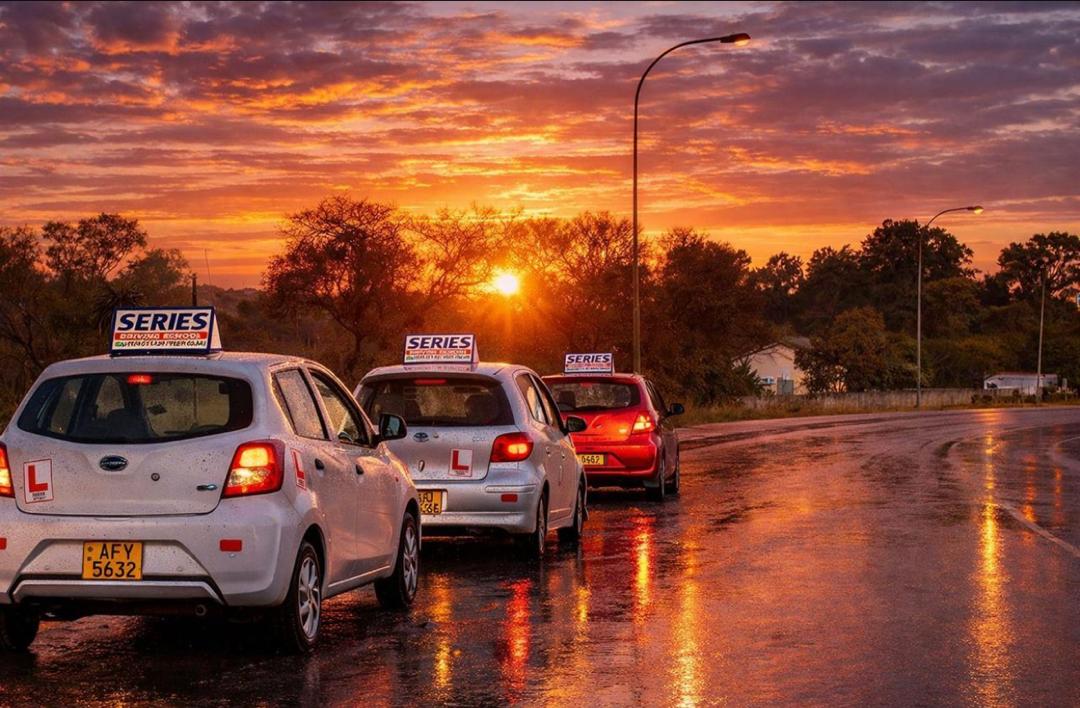 Series Driving School learner cars lined up on a wet road at sunset